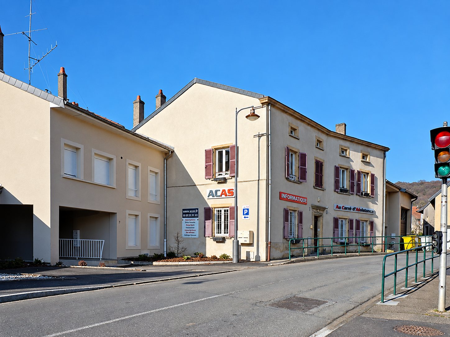 Immeuble d’angle clair aux volets bordeaux portant l’enseigne ACAS, au bord d’une rue de Saulny sous un ciel bleu.