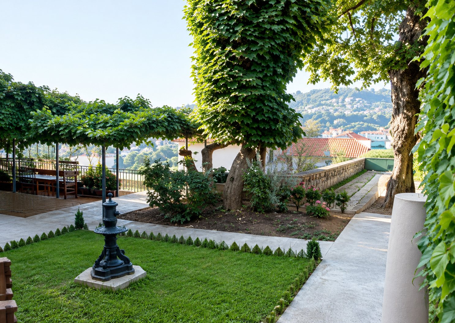 Un jardin aménagé avec une allée dallée, des arbres taillés et une pelouse, offrant une vue dégagée sur la ville en arrière-plan.