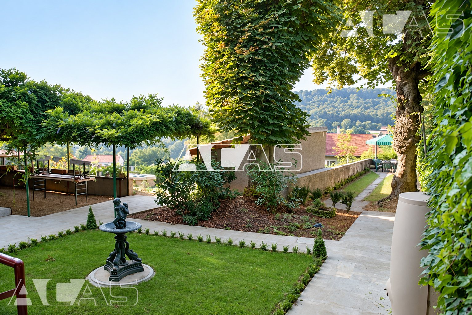 Un jardin soigné avec une petite fontaine en fonte sur la pelouse, une pergola couverte de végétation, des allées dallées et de grands arbres, avec des collines en arrière-plan.