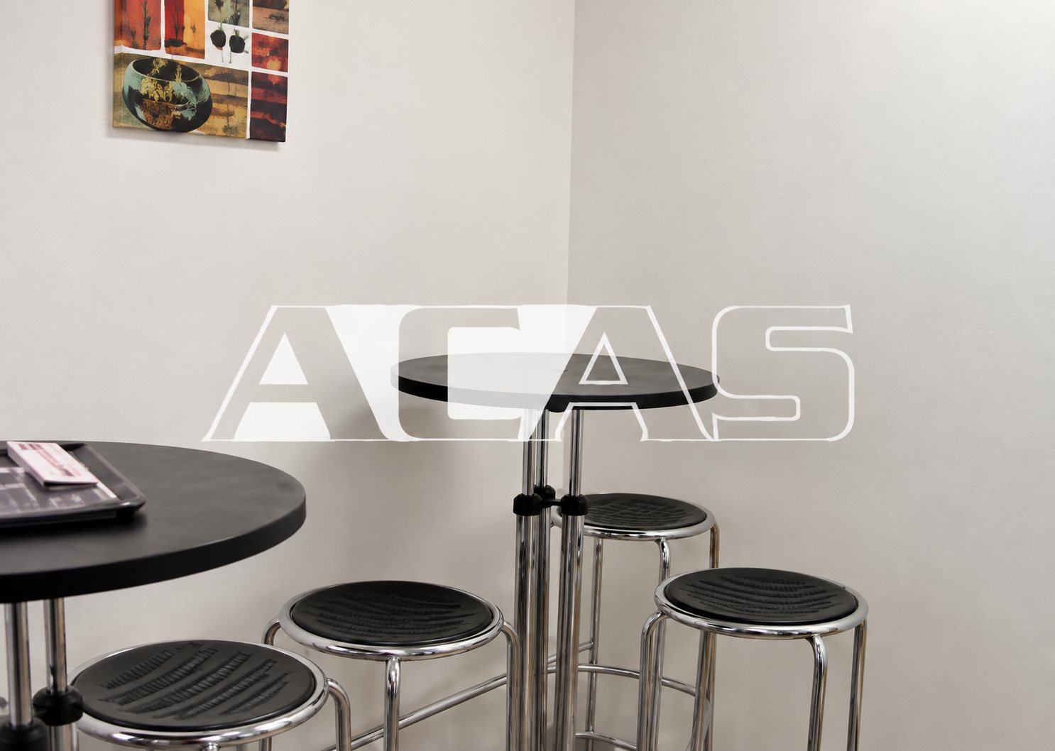 Table haute noire et tabourets métalliques dans un espace blanc.